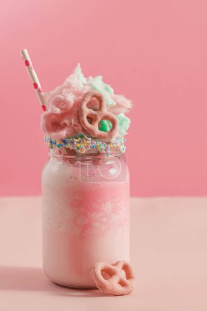 Milkshake in a glass jar covered with a cotton candy, pink background, pastel colors