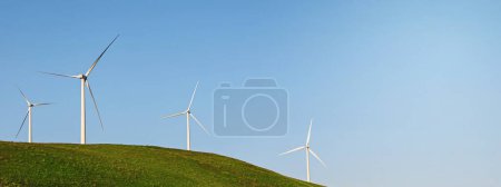 Bannière avec éoliennes sur la colline verte au-dessus du ciel bleu. Contexte énergétique durable