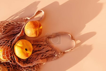 Photo for Ripe peaches in eco bag on pink background in natural light, top view - Royalty Free Image