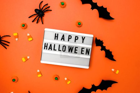 Photo for Traditional Halloween decor and candies on orange background with Happy Halloween on the lightbox - Royalty Free Image