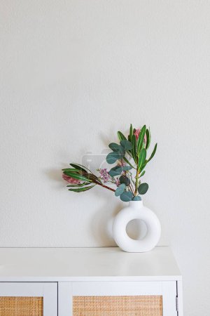 Minimalist home decor. Sandstone donut-shape vase on the dresser over the light grey wall
