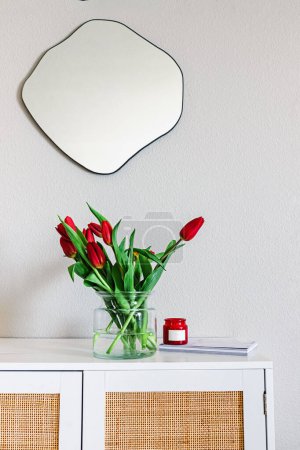 Photo for Minimalist modern living room with a fluid shape mirror on the wall and red tulips - Royalty Free Image