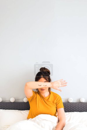 Photo for Woman sitting on the bed closing her face with her hand with eyes drawn on it. Sleep problem, insomnia, stress concept - Royalty Free Image
