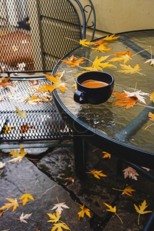 Photo for Cup of coffee standing on the patio table after the fall rain with lots of fallen yellow leaves - Royalty Free Image