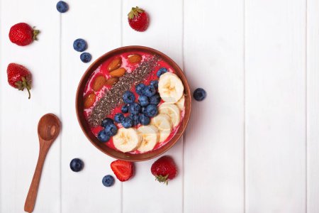 Photo for Strawberry smoothie bowl topped with berries and bananas on the white table. Healthy breakfast, top view - Royalty Free Image