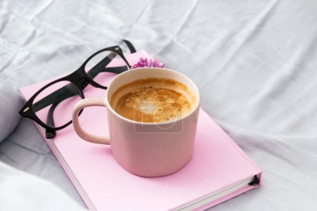Photo for Composition with pink mug with coffee, pink notepad or diary and glasses on the bed. - Royalty Free Image