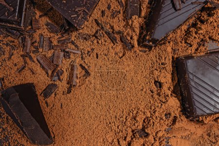 Rebanadas y afeitados de chocolate amargo oscuro dispersos en el fondo de cacao en polvo, vista superior