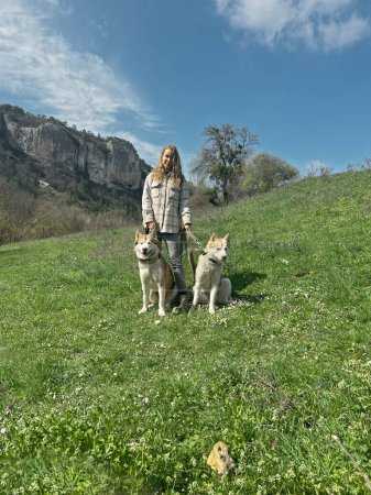 Foto de Mujer con dos perros malamute caminando por las montañas en el campo de primavera - Imagen libre de derechos