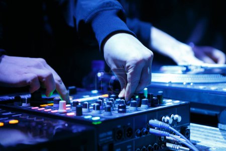 Foto de Dj tocando música en la fiesta en el club nocturno. Disco profesional jockey mezclando pistas musicales con dispositivo mezclador de sonido - Imagen libre de derechos