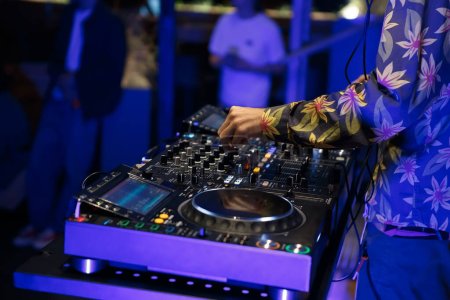 Téléchargez les photos : Party DJ mixant de la techno avec des tourne-disques CD modernes et un mixeur sonore à quatre canaux. Disque club jockey joue dans la boîte de nuit - en image libre de droit