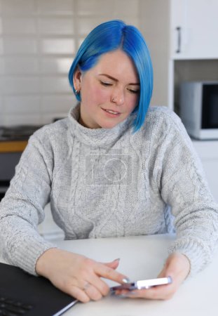 Téléchargez les photos : Blue haired woman browsing mobile app on smartphone. Cheerful Ukrainian femaler with dyed hair using modern mobile phone - en image libre de droit