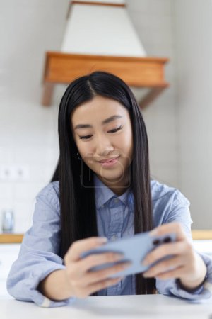 Photo for Gamer girl plays mobile game on smartphone. Cheerful Vietnamese BIPOC female playing online games with modern gadget - Royalty Free Image