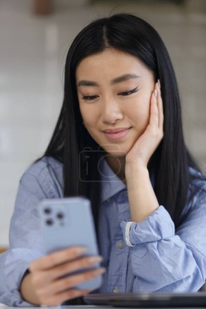 Téléchargez les photos : Beautiful POC girl from southeast asia browsing mobile app on smart phone. Portrait of young asian woman using modern blue mobile phone - en image libre de droit