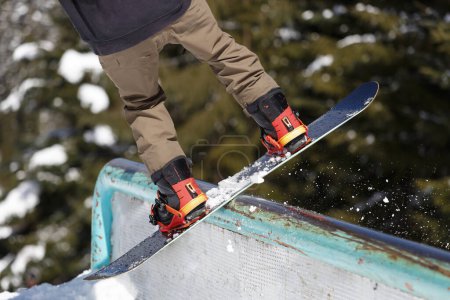 Téléchargez les photos : Snowboarder grinds on rail in winter park. Feet of snow board rider performing slide trick on winter sports competition in mountains - en image libre de droit