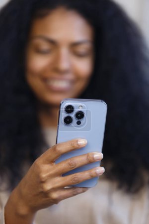 Téléchargez les photos : Happy BIPOC woman using blue smart phone with triple camera. Cheerful black female person browsing modern mobile phone - en image libre de droit