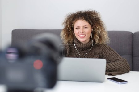 Téléchargez les photos : Video blogger woman films an educational course footage at home. Friendly white female with curly hair talks on video camera - en image libre de droit