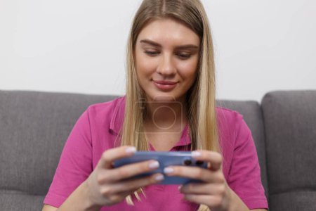 Téléchargez les photos : Happy gamer girl plays online games on modern smart phone. Cheerful blonde female person playing a videogame on gadget - en image libre de droit
