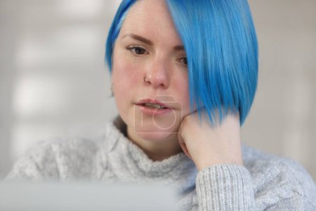 Téléchargez les photos : Close up portrait of millennial woman with bob haircut and dyed blue hair. Focused female person reading text from computer screen - en image libre de droit