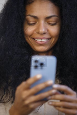 Téléchargez les photos : Happy black woman using smart phone. Portrait of cheerful BIPOC female in 30s browsing mobile app on a cell phone - en image libre de droit