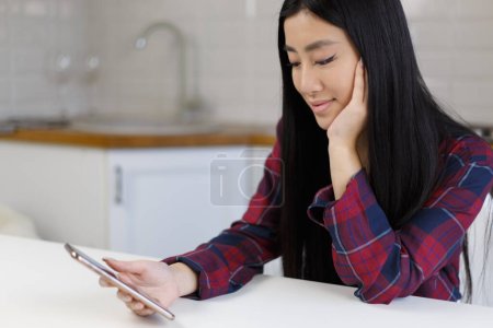 Photo for Beautiful asian girl browsing mobile app on modern smart phone. Cheerful Vietnamese POC using new golden mobile phone at home - Royalty Free Image