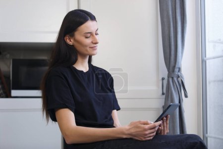 Photo for Beautiful brunette woman reading e-book on tablet computer. Attractive white female person in late 20s using modern gadget to browse internet - Royalty Free Image