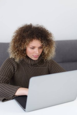 Photo for Beautiful curly woman working on notebook computer at home. Pretty young adult female person typing text on modern laptop - Royalty Free Image