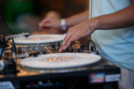 Photo for Club DJ scratching vinyl records with sound mixer and turntables. Professional disc jockey plays set on party - Royalty Free Image