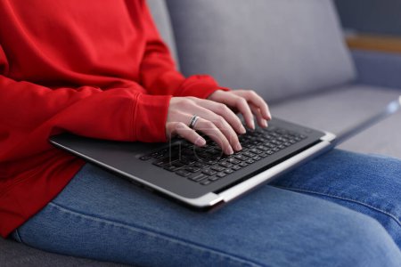 Téléchargez les photos : Closeup photo of female typing text on laptop keyboard on couch. Unrecognizable white woman works on modern notebook pc at home - en image libre de droit
