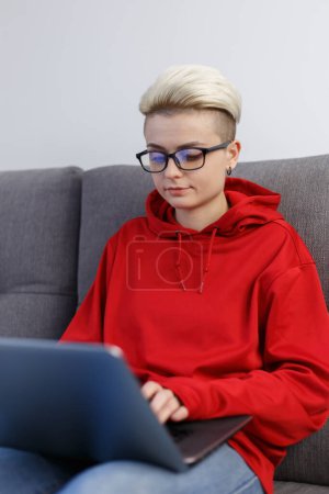 Foto de Mujer joven con el pelo corto que trabaja en la computadora portátil moderna en casa. Enfocado tom boy hembra con pelo corto escribiendo texto en la PC portátil - Imagen libre de derechos