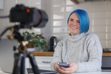 Téléchargez les photos : Blogueur joyeux parle sur la caméra vidéo. Femme blanche amicale aux cheveux bleus filmant un cours éducatif à la maison - en image libre de droit