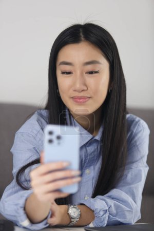 Foto de Beautiful Vietnamese girl using modern smart phone. Portrait of attractive POC woman browsing app on mobile phone - Imagen libre de derechos