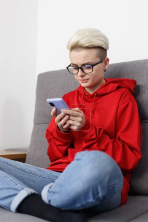 Téléchargez les photos : Young adult woman in glasses browsing mobile app on modern smart phone at home - en image libre de droit