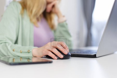 Téléchargez les photos : Adult woman working on a computer at home. Unrecognizable white female person clicking with wireless mouse on a laptop - en image libre de droit
