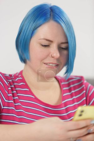 Téléchargez les photos : Portrait of white woman with blue hair using modern smart phone for communication. Millennial female person browsing mobile on the phone - en image libre de droit