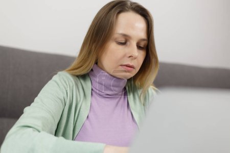 Téléchargez les photos : Femme blanche concentrée travaillant sur ordinateur à la maison. Femme adulte sérieuse faisant un travail à distance en ligne - en image libre de droit