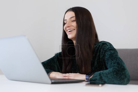 Téléchargez les photos : Happy young woman talking on web camera and laughing. Cheerful white female person speaking on video call at home - en image libre de droit
