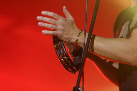 Téléchargez les photos : Musician playing on tambourine on rock concert stage. Hands of adult male singer holding a percussion musical instrument - en image libre de droit