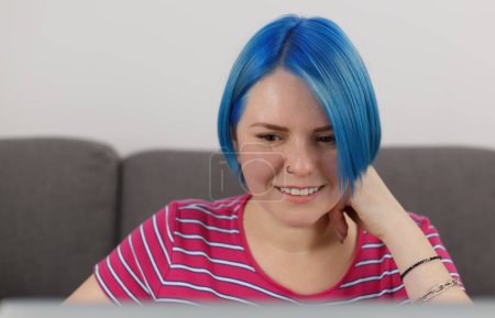 Téléchargez les photos : Beautiful white woman with blue hair studying online at home. Portrait of attractive young female person working on laptop with a smile - en image libre de droit