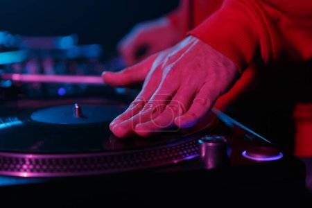 Téléchargez les photos : Hip hop dj scratching vinyl records on turntable. Club disc jockey playing music on party. Hand of disk jokey on a record in close up photo - en image libre de droit