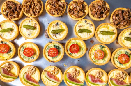 Foto de Flat lay photo of canape set cooked in bakery on metal tray. Big group of delicious snacks prepared for wine party in restaurant kitchen - Imagen libre de derechos