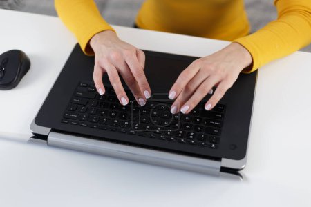 Foto de Young woman typing text on laptop keyboard. Overhead photo of female person working on modern notebook computer behind white desk. Focus on beautiful hands with French manicure - Imagen libre de derechos