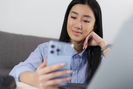 Photo for Young Vietnamese female person browsing app on blue mobile phone. Close up photo of Asian student girl using modern smart phone gadget - Royalty Free Image