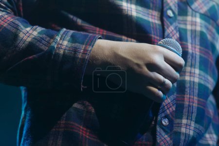 Photo for Hand of singer in classic plaid shirt holding microphone. Cool rapper with mic on concert stage. - Royalty Free Image