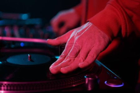 Foto de Hip hop DJ scratches vinyl disc on turntable in red stage lights. Hand of disc jockey scratching record disc in close up - Imagen libre de derechos