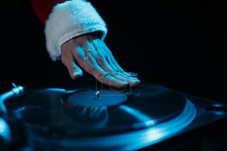 Photo for Santa DJ scratches vinyl record on turntable. Club disk jokey in red Christmas clothes plays music - Royalty Free Image