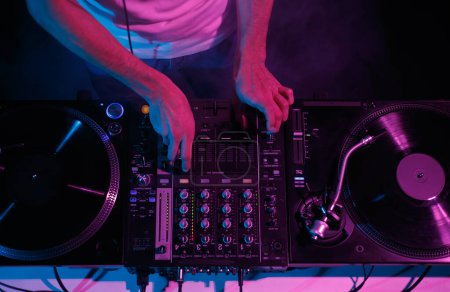 Club DJ mixing music with audio mixer and vinyl records. Disc jockey plays set with turntables on stage