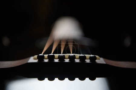 Téléchargez les photos : Fixing pegs on acoustic guitar bridge in close up. Beautiful black string instrument for professional guitarist - en image libre de droit