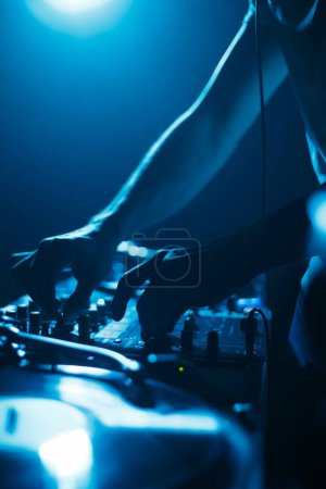 Téléchargez les photos : Club dj mélange de la musique mis sur la fête dans des lumières bleues vives. Silhouette de disc jockey sur scène - en image libre de droit