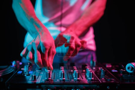 Foto de Club dj mixing music with sound mixer device. Professional disc jockey plays set on stage in night club - Imagen libre de derechos