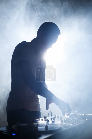 Téléchargez les photos : Silhoutte de DJ en fumée. Disque-jockey jouant de la musique sur scène en boîte de nuit - en image libre de droit